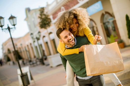Portrait of  young man holds young woman on his back , have fun and go to shopping