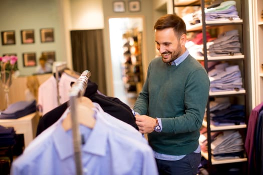 Portrait of a young cheerfull man looking at clothes to buy at shop