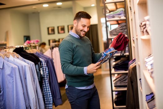 Portrait of a young cheerfull man looking at clothes to buy at shop