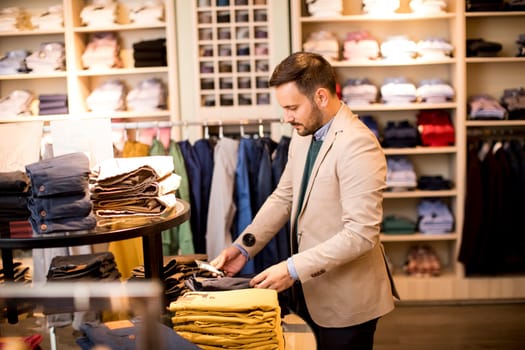 Handsome young man buying trousers in the store
