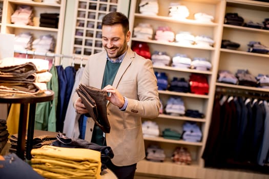 Handsome young man buying trousers in the store