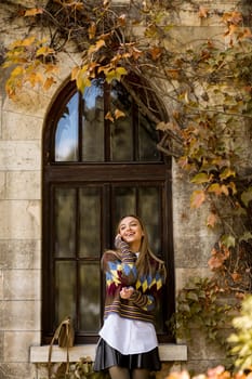 Pretty young woman standing with mobile phone on street at sunny autumn day