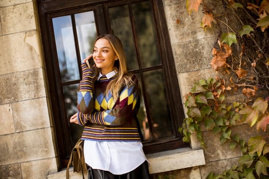 Pretty young woman standing with mobile phone on street at sunny autumn day