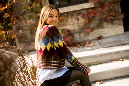 Pretty young woman sitting on the bench watching yellow leaves tree in the autumn park