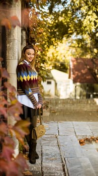 Pretty young woman standing outside at sunny autumn day