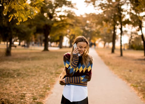 Pretty young woman walking in the autumn park and using a mobile phone