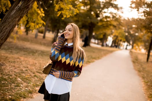 Pretty young woman walking in the autumn park and using a mobile phone