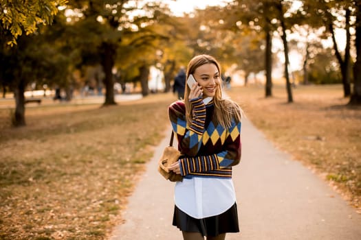 Pretty young woman walking in the autumn park and using a mobile phone