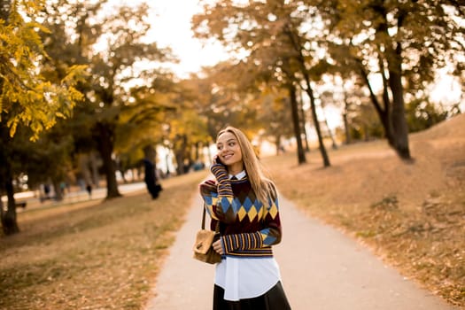 Pretty young woman walking in the autumn park and using a mobile phone