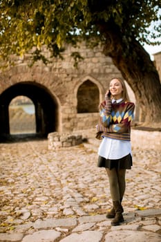 Pretty young woman standing with mobile phone on street at sunny autumn day