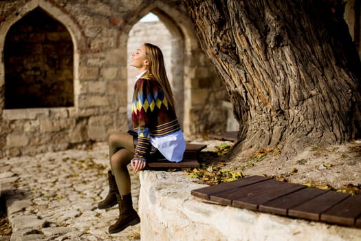 Pretty young woman sitting on the bench watching yellow leaves tree in the autumn park