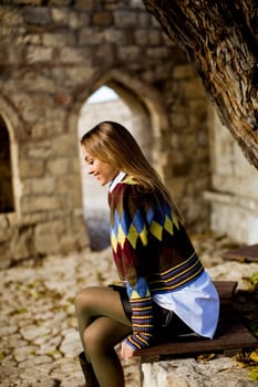 Pretty young woman sitting on the bench watching yellow leaves tree in the autumn park