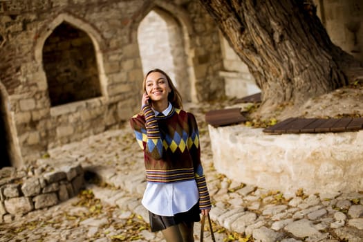 Pretty young woman walking in the autumn park and using a mobile phone
