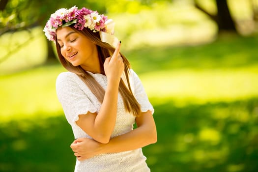 Portrait of young woman with wreath of fresh flowers on head in the park