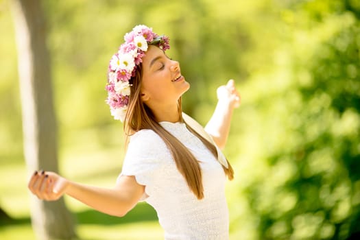 Portrait of young woman with wreath of fresh flowers on head in the park