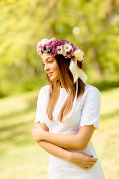 Portrait of young woman with wreath of fresh flowers on head in the park