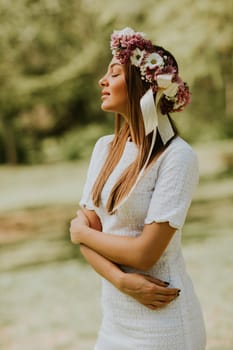 Portrait of young woman with wreath of fresh flowers on head in the park