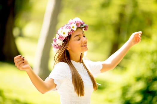 Portrait of young woman with wreath of fresh flowers on head in the park