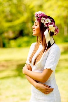 Portrait of young woman with wreath of fresh flowers on head in the park
