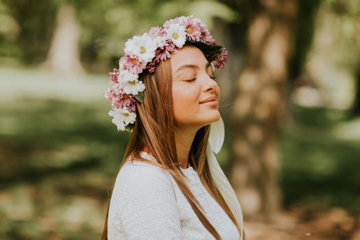 Portrait of young woman with wreath of fresh flowers on head in the park