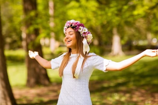 Portrait of pretty young woman with wreath of fresh flowers on head in the park