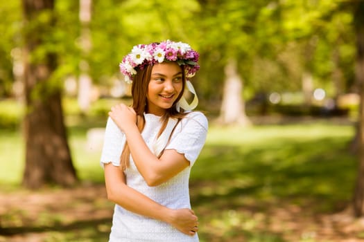 Portrait of pretty young woman with wreath of fresh flowers on head in the park