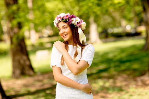 Portrait of young woman with wreath of fresh flowers on head in the park
