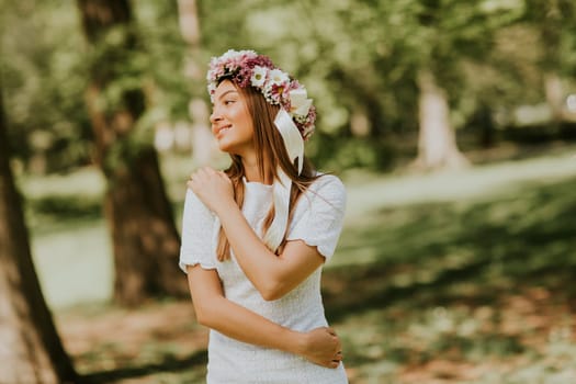 Portrait of young woman with wreath of fresh flowers on head in the park