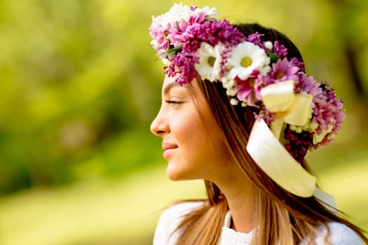 Portrait of young woman with wreath of fresh flowers on head in the park