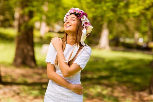 Portrait of pretty young woman with wreath of fresh flowers on head in the park