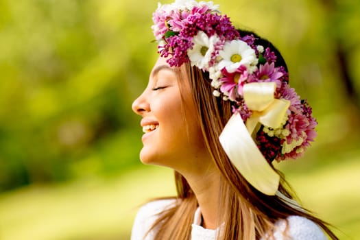Portrait of young woman with wreath of fresh flowers on head in the park