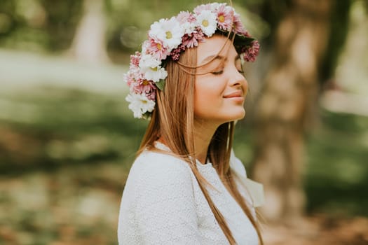 Portrait of young woman with wreath of fresh flowers on head in the park