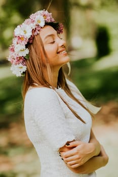 Portrait of young woman with wreath of fresh flowers on head in the park