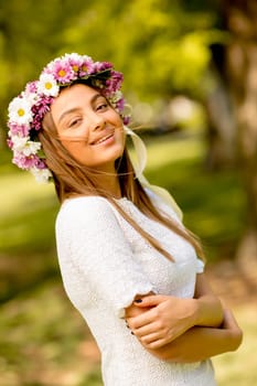 Portrait of young woman with wreath of fresh flowers on head in the park