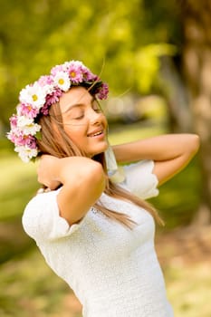 Portrait of young woman with wreath of fresh flowers on head in the park