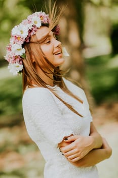 Portrait of young woman with wreath of fresh flowers on head in the park