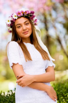 Portrait of pretty young woman with wreath of fresh flowers on head in the park