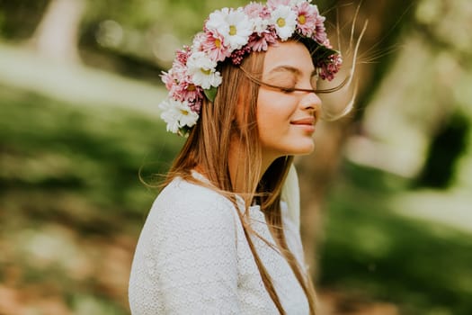 Portrait of young woman with wreath of fresh flowers on head in the park