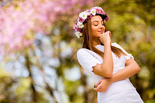 Portrait of pretty young woman with wreath of fresh flowers on head in the park