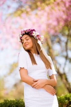 Portrait of pretty young woman with wreath of fresh flowers on head in the park