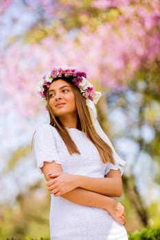 Portrait of pretty young woman with wreath of fresh flowers on head in the park