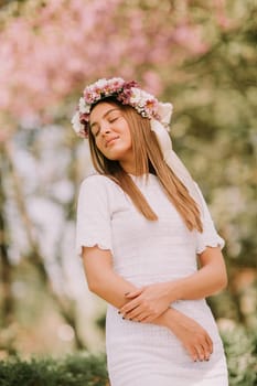Portrait of young woman with wreath of fresh flowers on head in the park