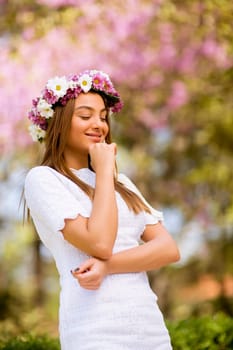 Portrait of pretty young woman with wreath of fresh flowers on head in the park