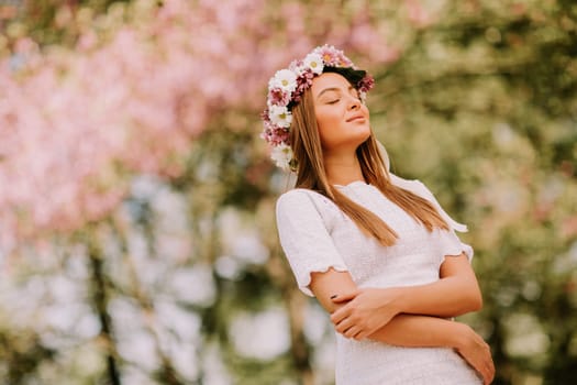 Portrait of young woman with wreath of fresh flowers on head in the park