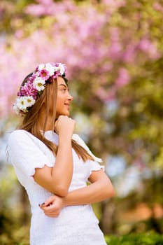 Portrait of pretty young woman with wreath of fresh flowers on head in the park