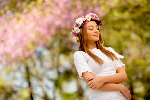Portrait of young woman with wreath of fresh flowers on head in the park