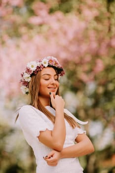 Portrait of young woman with wreath of fresh flowers on head in the park