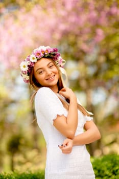 Portrait of young woman with wreath of fresh flowers on head in the park