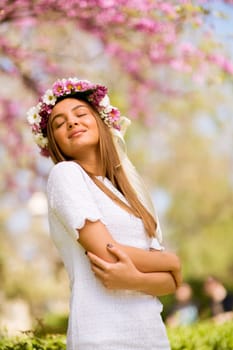 Portrait of pretty young woman with wreath of fresh flowers on head in the park