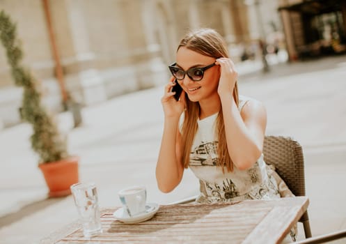 Pretty young woman using mobile phone in the cafe at summer